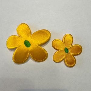 May include: Two yellow felt flower patches with green centers. The larger flower is about 3 inches wide and the smaller flower is about 2 inches wide.