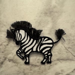 May include: Black and white embroidered iron-on patch of a zebra with a fringed mane and tail.