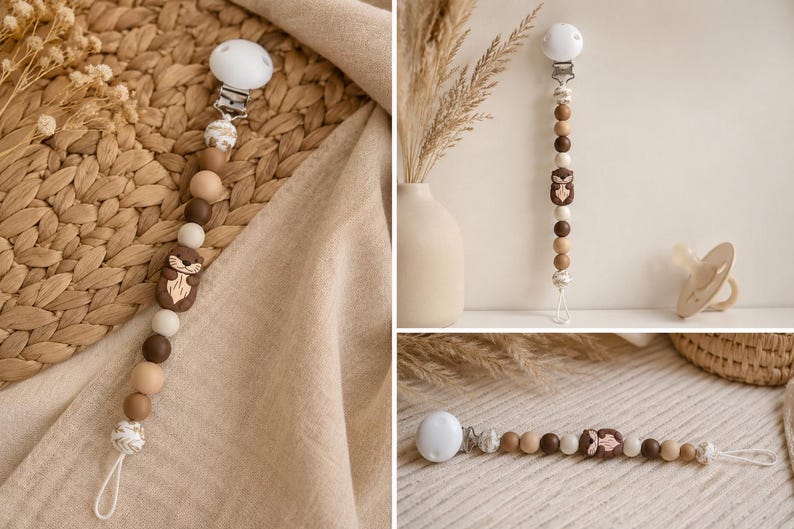 May include: A dummy clip featuring a series of round beads in shades of cream, tan, and dark brown, accented by a central brown silicone otter-shaped bead. The clip includes a white plastic fastener and a white cord loop at the bottom end.