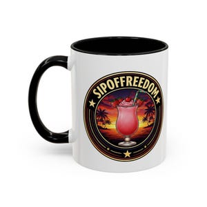 Puede incluir: Taza de cerámica blanca con asa e interior negros. La taza presenta un diseño circular con el texto "SIPOFFREEDOM" y una ilustración de un cóctel rosa con fresas, una pajita y un fondo de puesta de sol.