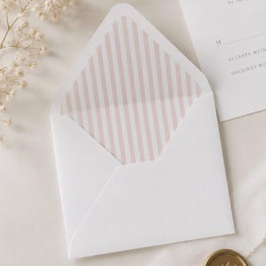 May include: A white envelope with a pink and white vertical striped liner, accompanied by a response card featuring the text KINDLY REPLY by the first of, M, ACCEPTS WITH, and DECLINES WITH, alongside a gold wax seal with a floral design.