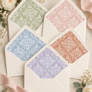 May include: Five cream-colored envelopes with open flaps, each featuring a unique interior liner pattern. The liners display a white symmetrical botanical design against backgrounds of sage green, dusty pink, light blue, terracotta, and lavender.