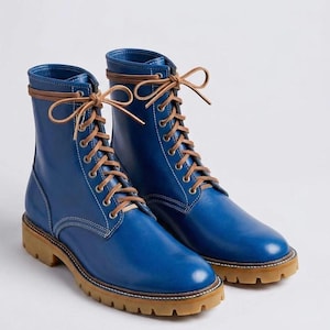 Puede incluir: Un par de botas de cuero azul con cordones, acabado liso, cordones de cuero color canela, ojales de metal plateado, costuras blancas en contraste y una suela de goma gruesa y texturizada en color canela con tacón definido.