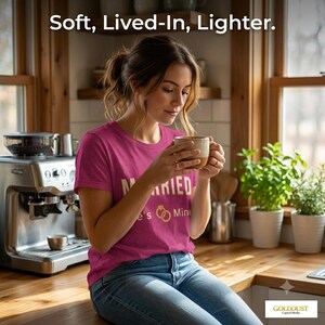 May include: A magenta short-sleeved t-shirt with the text "MARRIED" and a ring graphic printed in white and gold. The shirt features a crew neckline and a standard fit. The text "Soft, Lived-In, Lighter." is displayed at the top of the image.