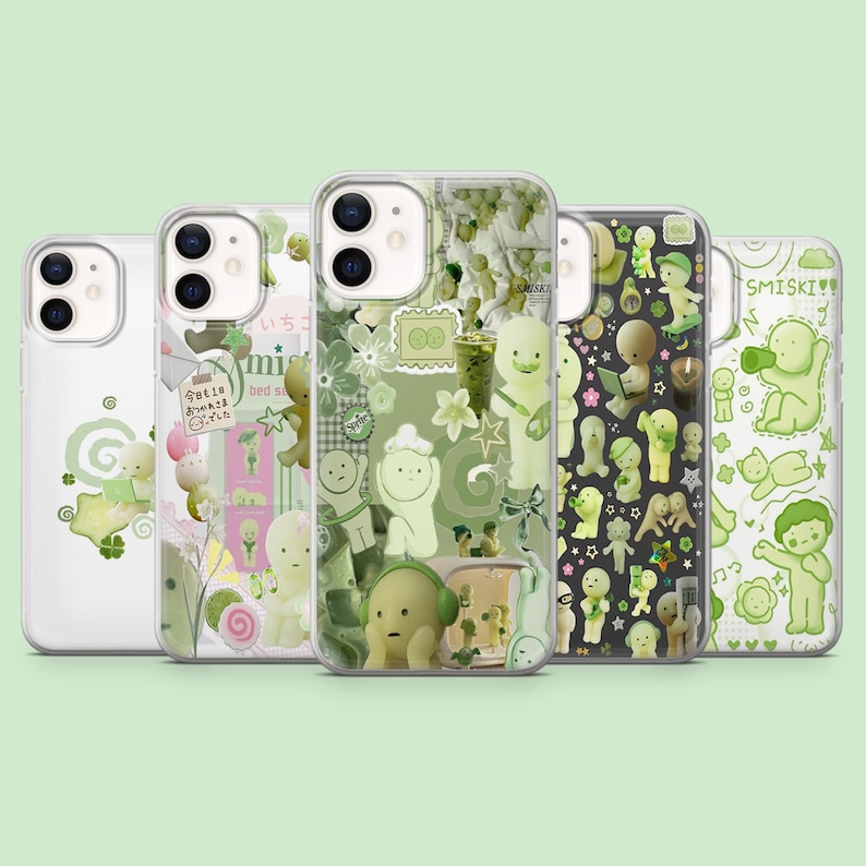 May include: A collection of five clear phone cases with various designs. The cases feature green and white illustrations of cartoon figures, flowers, and text. One case has the text "SMISKI!!".