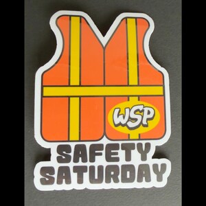 May include: A die-cut sticker featuring an orange safety vest with vertical and horizontal yellow reflective stripes. An oval yellow badge on the lower right displays the letters WSP in white. Below the vest, the text SAFETY SATURDAY appears.