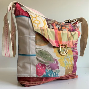 May include: A patchwork style shoulder bag with a long strap. The bag is made of different fabrics with floral and geometric patterns in shades of pink, red, yellow, green, blue, and brown. The bag has a gold buckle closure.