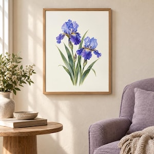 May include: A framed botanical wall art print featuring two vibrant blue iris flowers with yellow centers and long green leaves. The illustration is set against a plain off-white background and enclosed in a simple light-toned wooden frame.