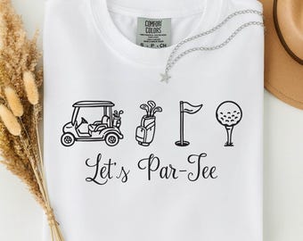 May include: A white t-shirt featuring a black graphic print of a golf cart, a golf bag, a flag, and a golf ball on a tee. Below the icons, the text reads Let's Par-Tee in a black cursive font. The shirt has a crew neckline and a Comfort Colors label.