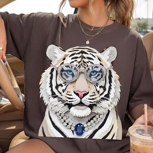 Könnte beinhalten: Ein dunkelbraunes Kurzarm-T-Shirt mit einem großen Grafikdruck eines weißen Tigers, der eine runde, mit Kristallen besetzte Brille und eine zweireihige Diamantkette mit einem ovalen blauen Edelsteinanhänger in der Mitte trägt.