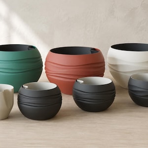 May include: A collection of seven round planters in various sizes and colors, including teal, terracotta, white, and charcoal gray. Each planter features a textured, wavy exterior surface and a smooth interior rim with a small integrated drainage notch.