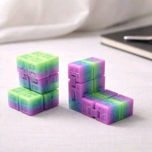 May include: Two colorful fidget cubes in shades of green, purple, and blue. The cubes are arranged in different configurations, showcasing their flexible design. The background is a soft, neutral color.