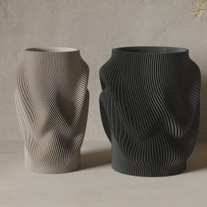 May include: Two cylindrical vases with a distinct vertical ribbed texture and a wavy, undulating surface pattern. One vase is light beige, and the other is dark charcoal grey. Both vessels feature a wide, open top and a flat, stable base.