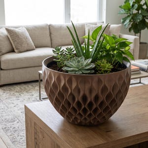 May include: A round, bronze-colored planter with a textured, vertical wave pattern on the exterior. The planter is filled with a variety of green succulents and leafy plants, including an aloe vera plant and a central rosette-shaped succulent.