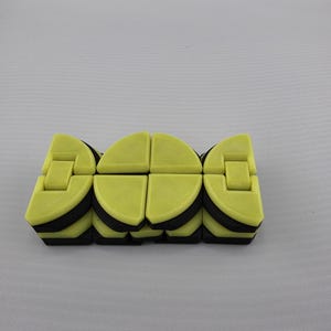 May include: A yellow and black fidget toy, composed of several connected, semi-circular segments. The toy is designed to be manipulated and played with, offering a tactile experience. The segments are a bright yellow with black accents.