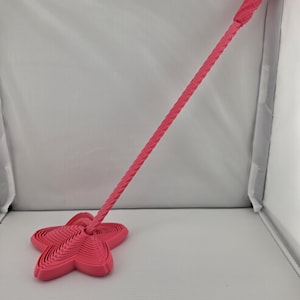 May include: A bright pink wand featuring a five-pointed star at the base with a layered, concentric design. The handle is long, slender, and has a twisted, spiral texture that extends from the star base up to the top end of the wand.