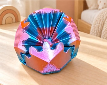 Puede incluir: Un Gear Rhombo Fidget Toy – Giant Transforming Mechanical Fidget. Este objeto geométrico de múltiples facetas presenta un degradado vibrante de colores azul metálico, morado y naranja con bordes en forma de engranajes entrelazados y una superficie texturizada.