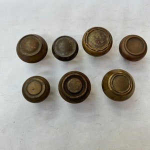 May include: Seven antique brass cabinet knobs with various designs. The knobs are round and have a slightly raised center. Some of the knobs have a simple design, while others have a more intricate design.