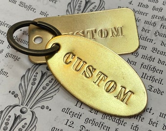 May include: Two gold-colored metal keychains with the word "CUSTOM" engraved on them. The keychains are oval and rectangular in shape.