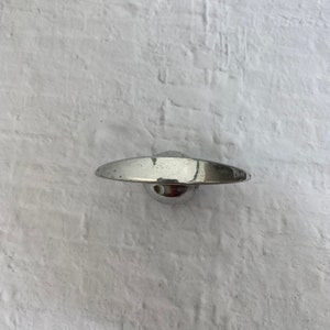 May include: A silver-toned, round, decorative door knob with a flat, oval-shaped handle.