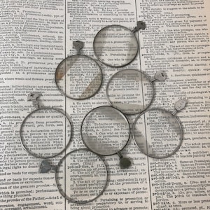 Puede incluir: Primer plano de varias lupas con marcos y mangos de metal. Las lupas están colocadas sobre una página de un diccionario con la palabra "prominent" resaltada. La página del diccionario está llena de texto sobre la palabra "prominent" y sus diversas definiciones.