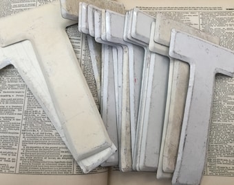 May include: A stack of white painted metal letter T's, some are slightly chipped, on top of a vintage dictionary.
