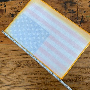 Pu&ograve; includere: Un patch di bandiera americana in tessuto bianco con un bordo giallo. Il patch &egrave; largo circa 23 cm e alto 15 cm.