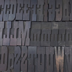 May include: A close-up of a collection of vintage wooden letterpress printing blocks. The blocks are arranged in rows and columns, and they feature the letters C, D, E, F, I, L, M, and O. The blocks are made of dark wood and have a worn, rustic appearance.