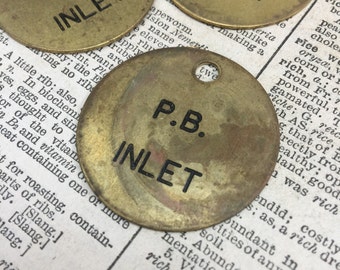 May include: Three round brass tags with the text "P.B. INLET" printed in black. The tags have a hole in the centre.