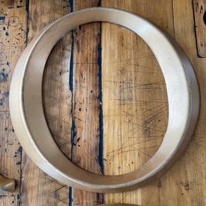 May include: A large, gold-colored, decorative circle made of metal. The circle is thick and has a rounded edge. It is sitting on a wooden surface.