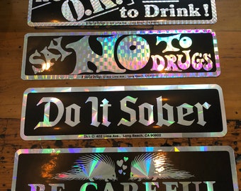 Peut inclure: Quatre autocollants holographiques noirs et argentés avec du texte blanc. Les autocollants indiquent "It's OK. Not to Drink!" "Say No to Drugs" "Do It Sober" et "Be Careful". Le dernier autocollant représente une paire de porcs-épics avec des cœurs.