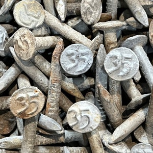 May include: A close-up of a pile of galvanized nails with the number "35" stamped on the heads. The nails are arranged in a random pattern, with some of the heads facing up and others facing down.