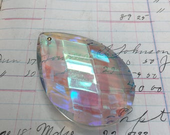 Puede incluir: Un prisma de cristal iridiscente transparente con una tapa de metal dorado. El prisma tiene forma de lágrima y presenta un diseño facetado.