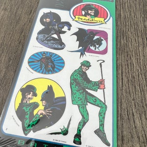Peut inclure: Un ensemble d'autocollants Batman et The Riddler. Les autocollants pr&eacute;sentent divers personnages des bandes dessin&eacute;es de Batman, notamment Batman, Robin, The Riddler et The Penguin. Les autocollants sont imprim&eacute;s sur du papier blanc avec une finition brillante.