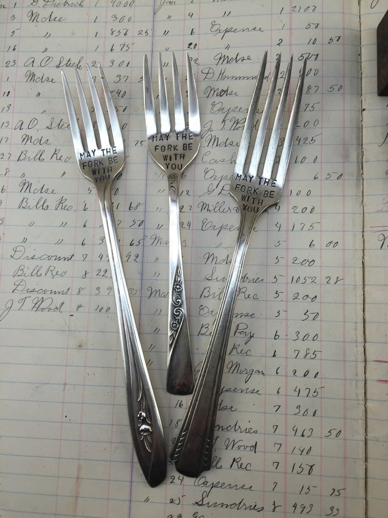 May include: Three silver forks with engraved messages. The forks have ornate designs on the handles. The messages read "May the fork be with you".