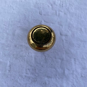 May include: A round, gold-toned cabinet knob with a raised, circular design.
