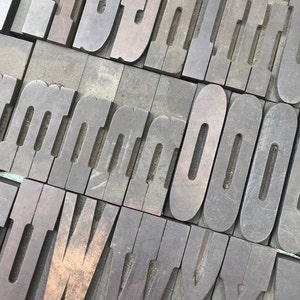May include: A collection of vintage wooden letterpress printing blocks. The blocks are arranged in a diagonal pattern and feature the letters F, G, H, I, J, K, L, M, N, O, U, V, W, X, Y, and Z.