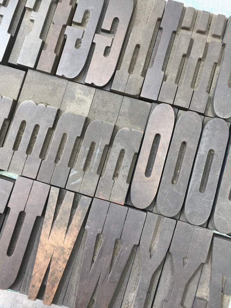 May include: A collection of vintage wooden letterpress printing blocks. The blocks are arranged in a diagonal pattern and feature the letters F, G, H, I, J, K, L, M, N, O, U, V, W, X, Y, and Z.