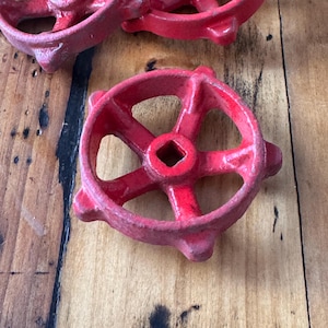 Peut inclure: Quatre poignées de vanne en métal rouge avec un trou carré au centre. Les poignées ont un design en étoile avec cinq points.