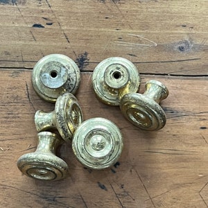 May include: Six gold-toned cabinet knobs with a variety of designs. The knobs are on a wooden surface.