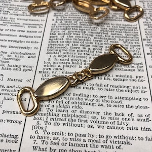 May include: Gold-toned metal chain links with oval-shaped connectors. The chain is on a page of a dictionary with text about the word "miss".