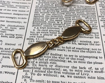Puede incluir: Cadenas de metal dorado con conectores ovalados. La cadena está sobre una página de un diccionario con texto sobre la palabra "miss".