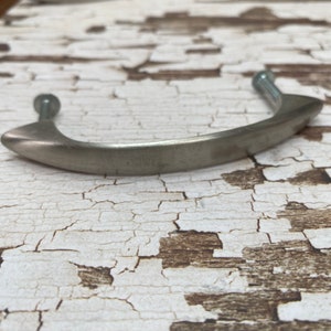 May include: A brushed nickel cabinet pull with a curved handle design. The hardware features two mounting screws and a smooth, matte finish. The pull is designed for easy installation and adds a modern touch to cabinetry.