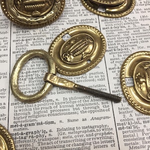 May include: A close-up of a group of antique brass oval-shaped door knobs with decorative details. The knobs have a beaded edge and a raised design in the center. The knobs are arranged on a page of a dictionary with the word "meta" highlighted.