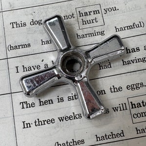 May include: A silver-colored, five-pointed star-shaped knob with a round center hole. The knob is resting on a page of a book with text that reads "This dog not harm you. hurt harming harmful".