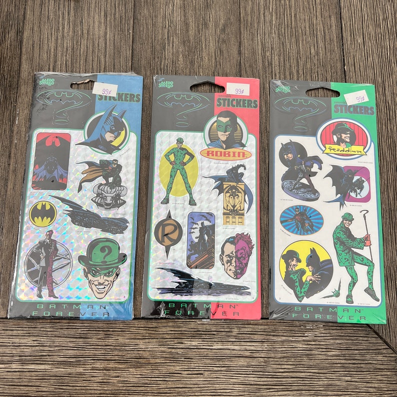 Peut inclure: Trois paquets d'autocollants Batman Forever. Chaque paquet pr&eacute;sente un personnage diff&eacute;rent du film&nbsp;: Batman, Robin et l'Homme-Myst&egrave;re. Les autocollants sont holographiques et ont un fond argent&eacute;. Les paquets sont &eacute;tiquet&eacute;s avec le titre du film et le nom du personnage.
