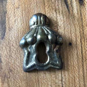 Könnte beinhalten: Ein antiker Schlüsselschlitz-Abdeckungen aus Messing mit einem verzierten Design. Die Abdeckung hat einen abgenutzten, gealterten Look mit einer angelaufenen Oberfläche.