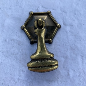 Könnte beinhalten: Ein goldfarbener Metall-Schrankknauf mit sechseckiger Basis und einem Schachstück-förmigen Griff.