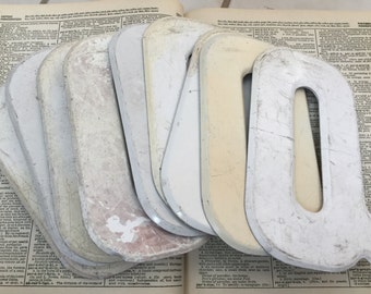 Può includere: Un set di lettere in legno dipinte di bianco, ciascuna a forma della lettera "O". Le lettere sono impilate l'una sull'altra, e alcune sono leggermente scheggiate o usurate.