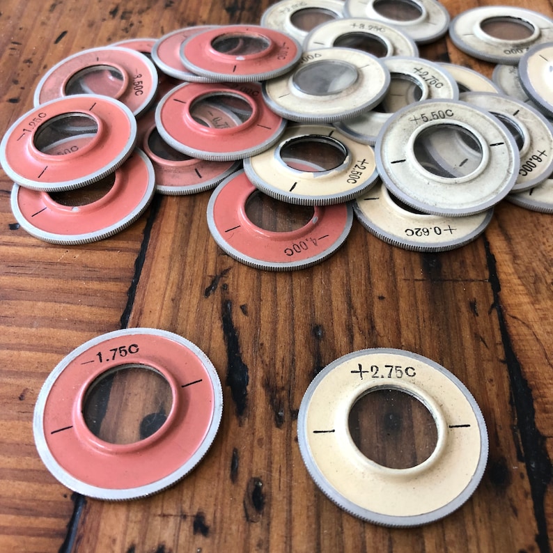 以下が含まれることがあります： 白と赤のマークが付いた丸い金属製の測定工具のセット。工具には数字と「C」の文字が記されています。